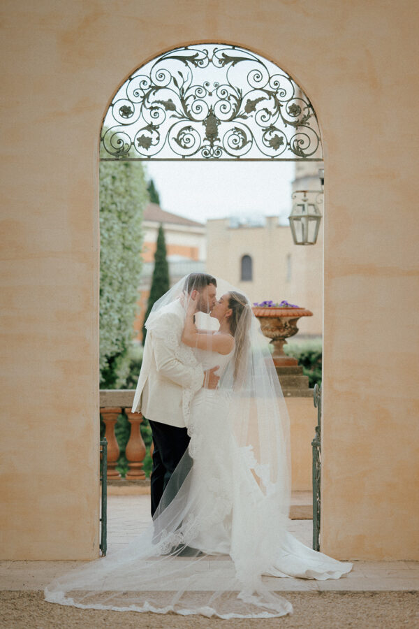 Bride and groom kissing beneath the bridal veil, framed by an archway at Villa Aurelia in Rome, by Miguel Ponte